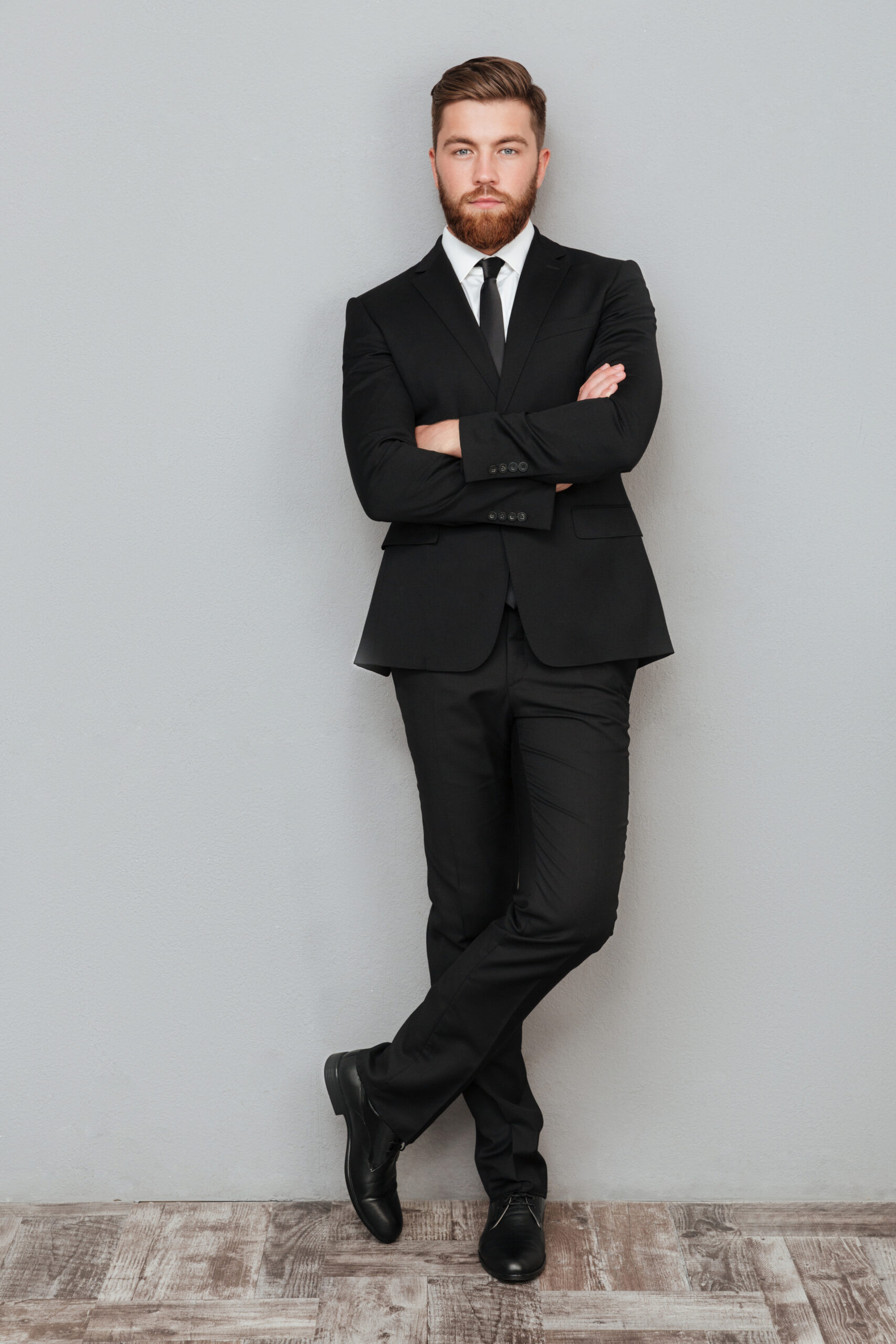 Full length portrait of a handsome successful businessman in suit posing with arms folded while standing isolated over gray background